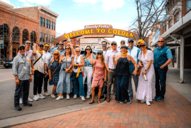A group of Golden History Tours participants poses in front of Golden, Colorado's street-spanning "Welcome to Golden" sign.